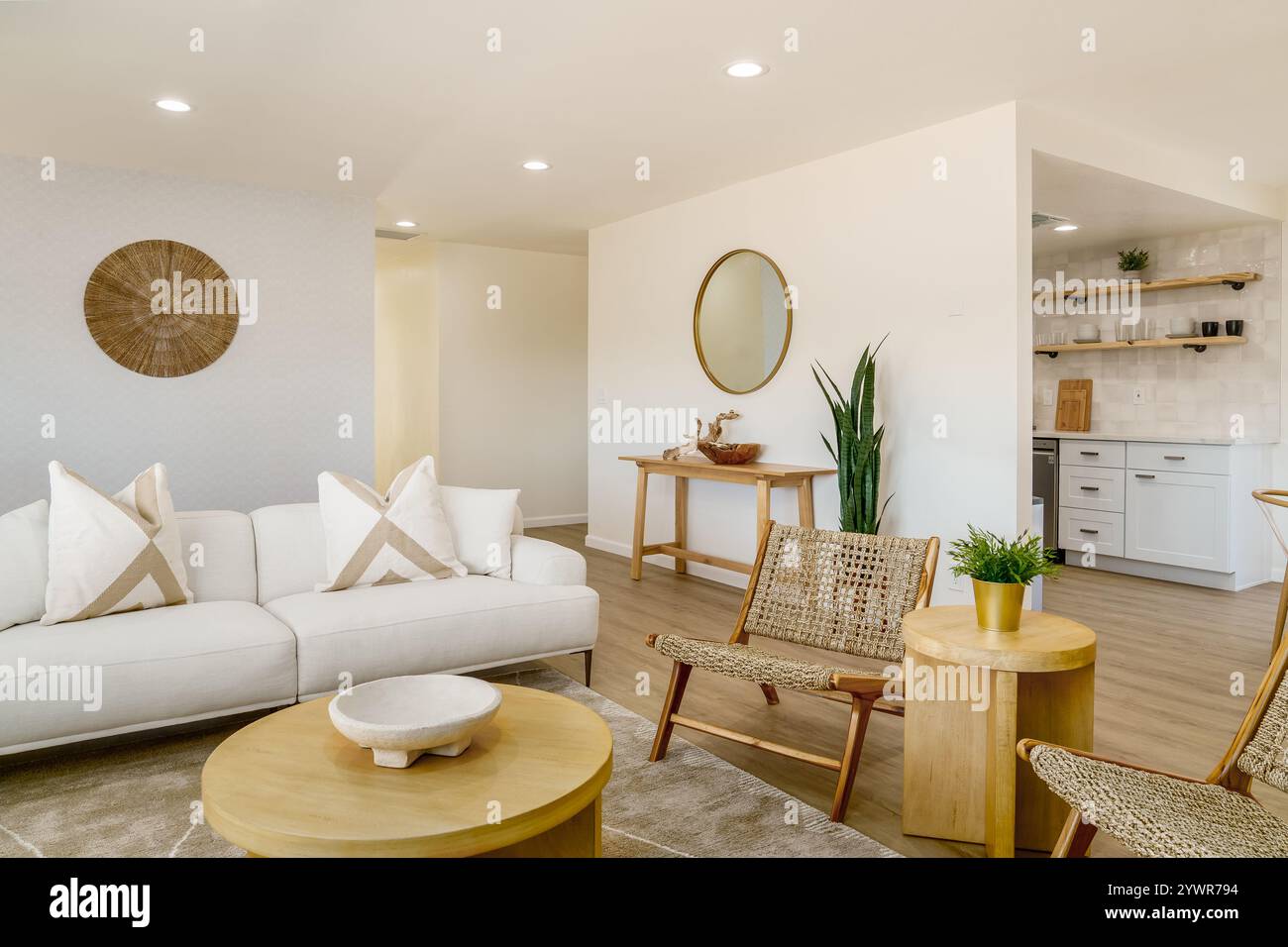 Helles, wüstendes Wohnzimmer mit weißem Sofa, hellen Holzmöbeln, gewebten Stühlen und einer neutralen Farbpalette. Stockfoto