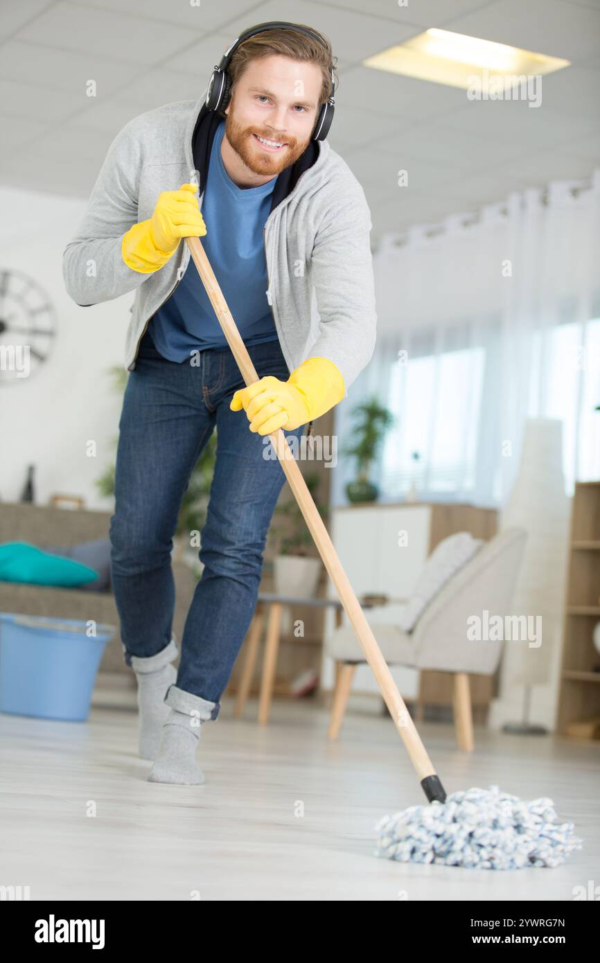 Glücklicher Mann mit Wischmopp und Eimer, der zu Hause den Boden reinigt Stockfoto