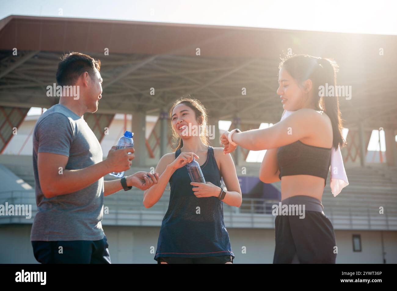 Eine Gruppe asiatischer Läufer genießt nach dem Training in einem Stadion an einem hellen, sonnigen Tag eine Unterhaltung, während sie sich auf einer Laufstrecke ausruhen. Personen und Stockfoto