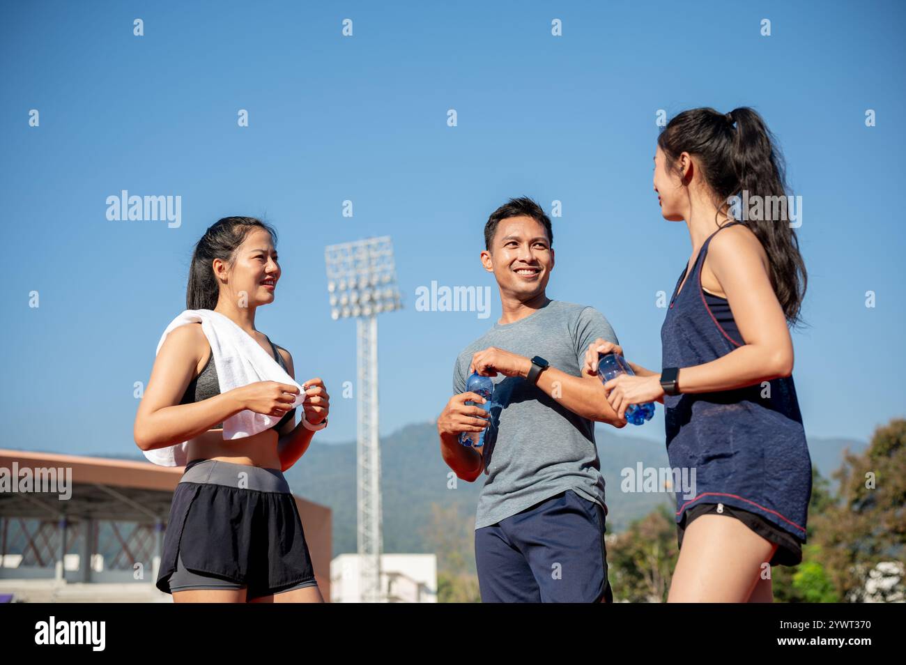 Eine Gruppe asiatischer Läufer genießt nach dem Training in einem Stadion an einem hellen, sonnigen Tag eine Unterhaltung, während sie sich auf einer Laufstrecke ausruhen. Personen und Stockfoto