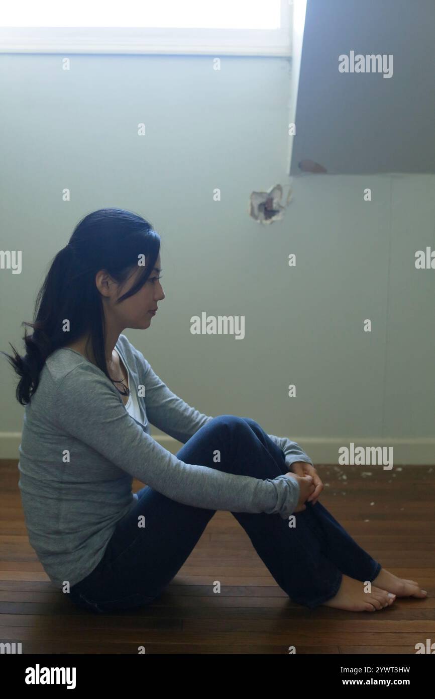 Einsame Frau, die in einem schwach beleuchteten Raum sitzt Stockfoto