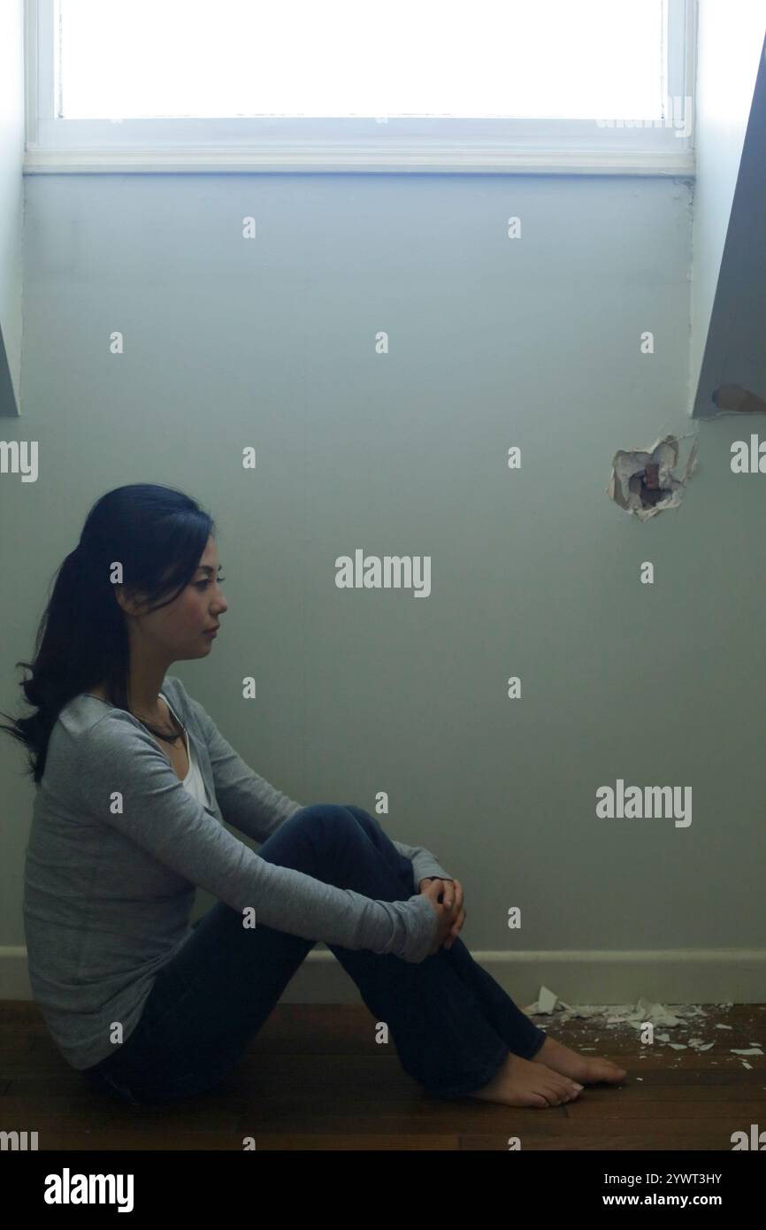 Einsame Frau, die in einem schwach beleuchteten Raum sitzt Stockfoto