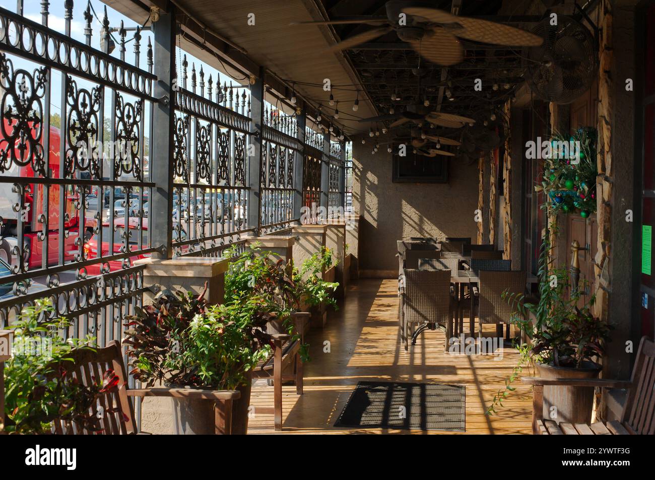 Führen Sie die Schlangen in einen Sitzbereich. Mehrere Tische, Stühle, Deckenventilatoren. Black Metal Bars an der Stadtstraße mit Verkehr. Sonnenschein und Stockfoto