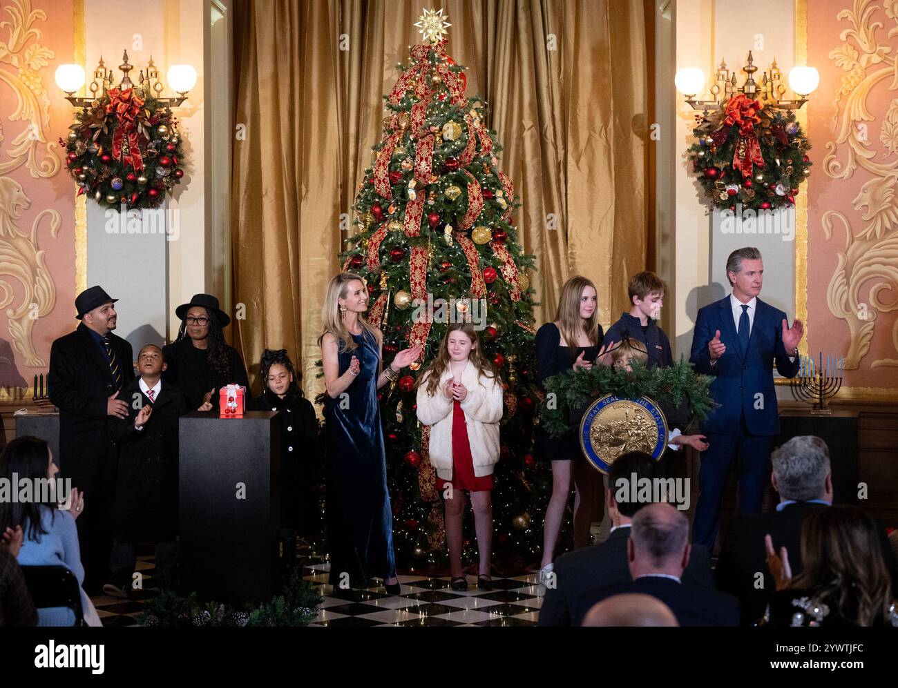 Sacramento, CA, USA. Dezember 2024. Carter Morris, 9 Jahre alt, mit seiner Familie, Lynne und Karl Morris, und Schwester Samira, hören das Lied Oh Happy Day, gesungen vom Oakland Interfaith Gospel Choir mit Gouverneur Gavin Newsom, erster Partner Jennifer Siebel Newsom und ihren Kindern während des 93. Jährlichen California State Capitol Tree im State Capitol am Mittwoch, 11. Dezember 2024, in Sacramento. Carter Morris wurde vom Central Valley Regional Center (CVRC) ausgewählt, um den Baum zu beleuchten und die mehr als 450.000 Kalifornier mit intellektuellen und entwicklungsbedingten Behinderungen zu repräsentieren, die s erhalten Stockfoto