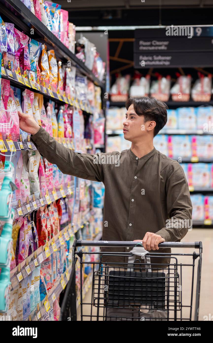 Chiang Mai, Thailand - 09. Dezember 2024: Ein gutaussehender asiatischer Mann, der in einem Supermarkt einkauft, Haushaltsartikel kauft und Produkte aus dem Regal auswählt. Nachteile Stockfoto