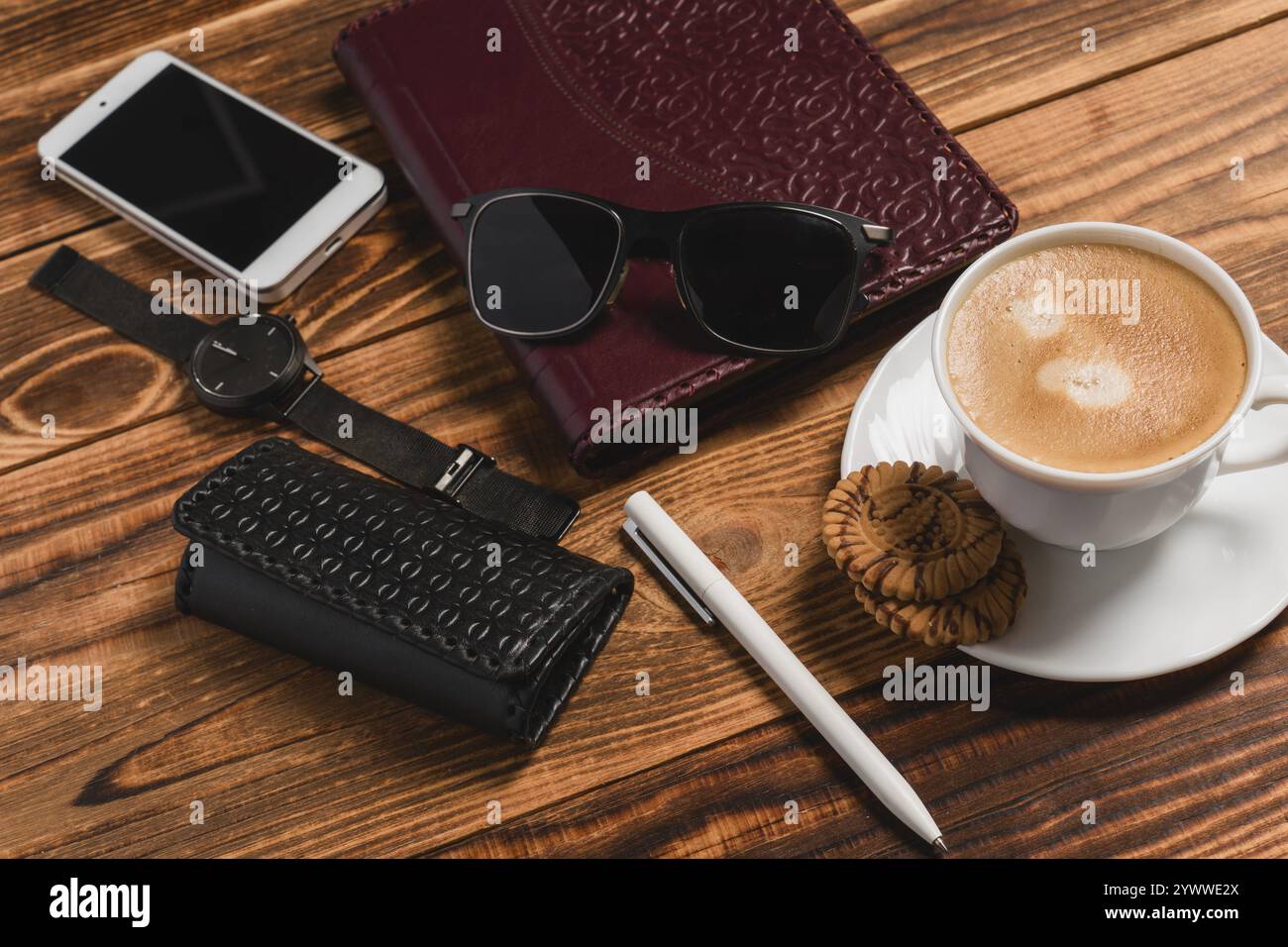 Eine weiße Tasse Kaffee, Smartphone, Waisen und Tagebuch auf Holztisch mit Morgensonne. Planung des Tageskonzepts. Stockfoto