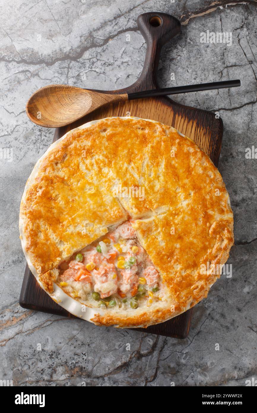 Topf Pie mit rotem Fisch, grünen Erbsen, Karotten, Mais und Sahnesauce mit knusprigem Teig in einer Auflaufform auf dem Tisch. Vertikale Draufsicht f Stockfoto