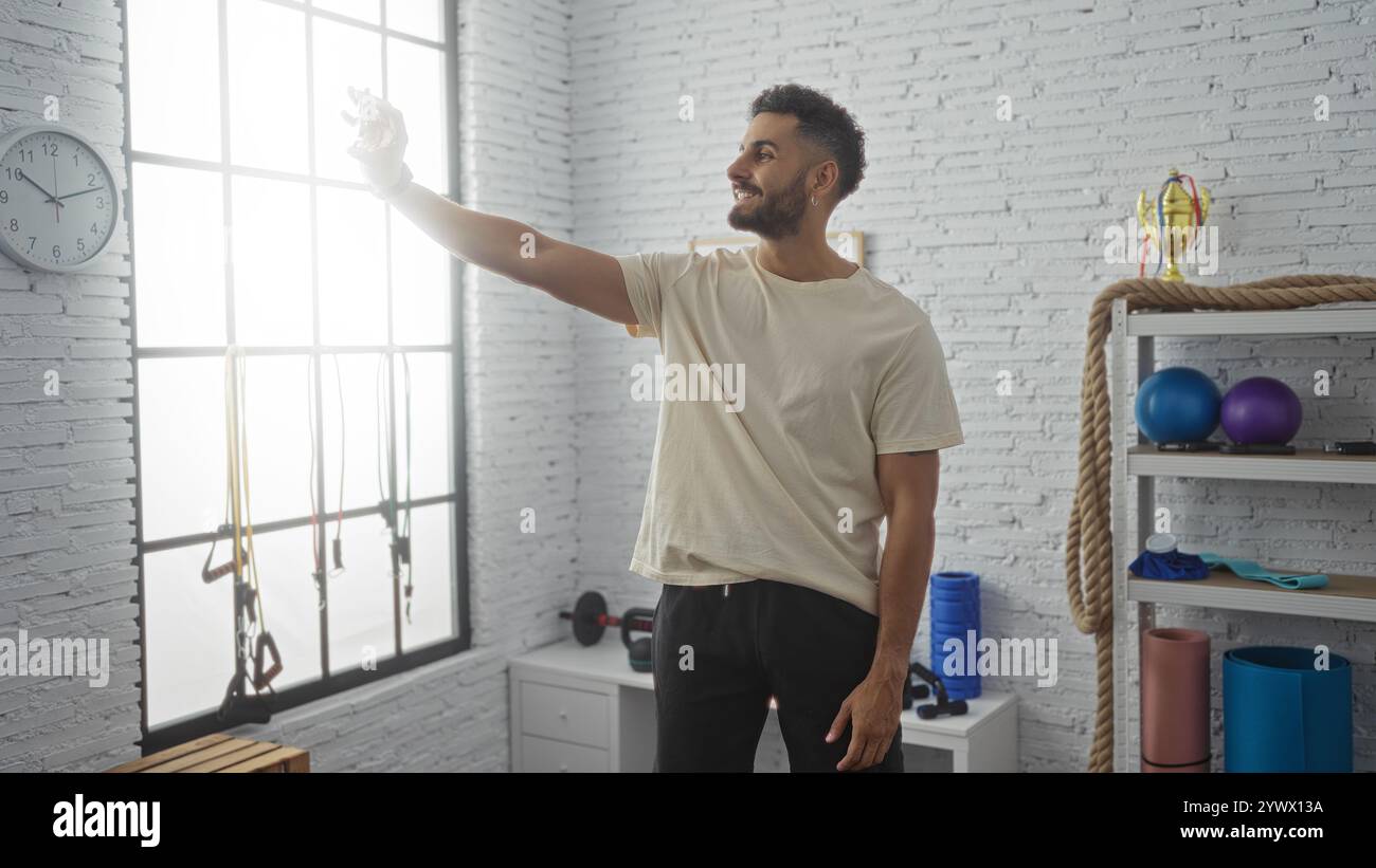Junger gutaussehender hispanischer Mann, der ein Selfie in einer Turnhalle mit Trainingsgeräten im Hintergrund macht Stockfoto