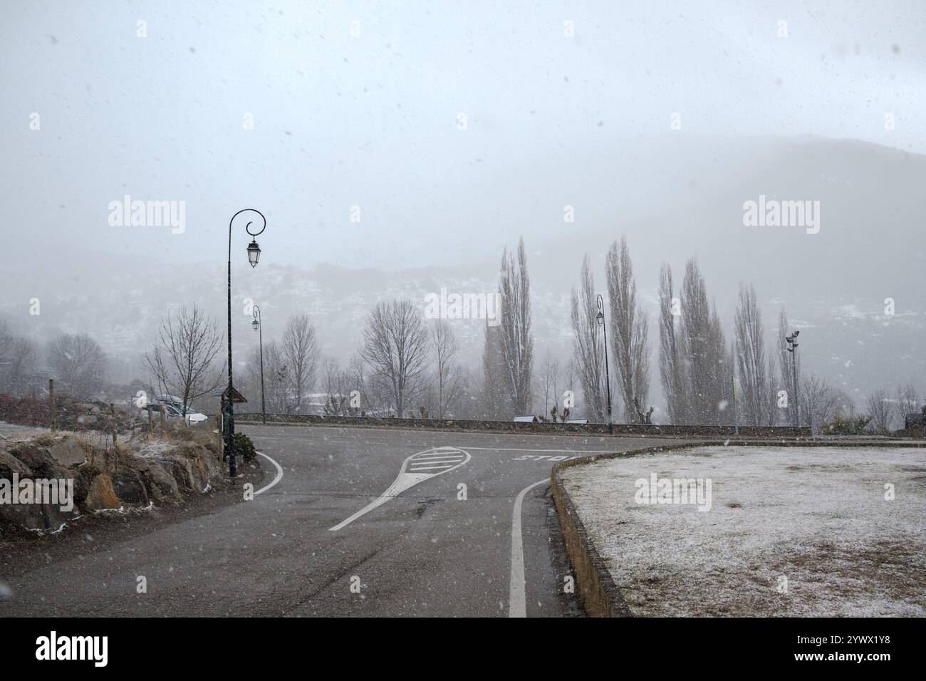 Schneeflocken fallen sanft über das Vall de Boí und schaffen eine ruhige Winterlandschaft. Blattlose Bäume säumen die Straße, während eine weiche weiße Beschichtung den Blattbaum bedeckt Stockfoto