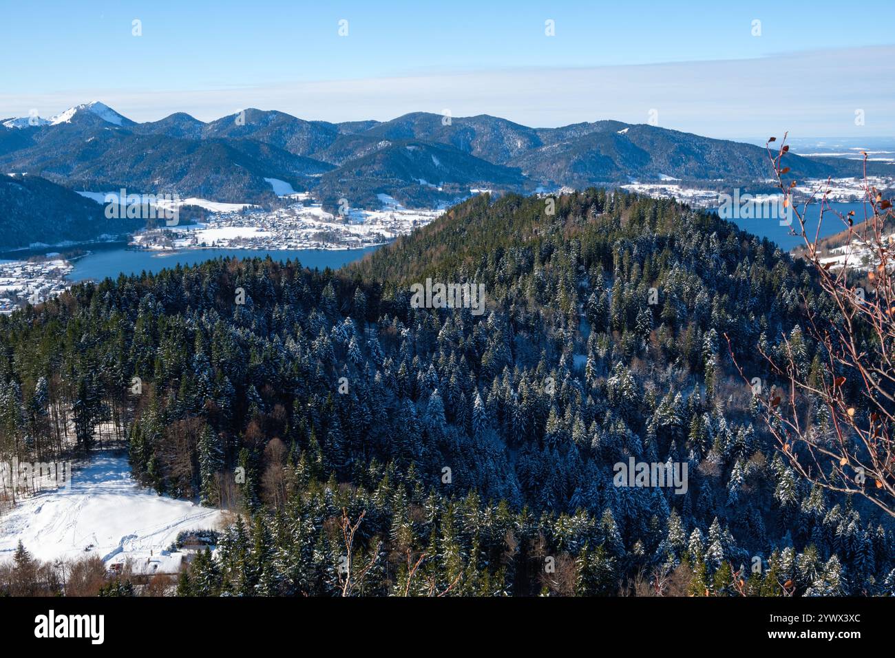 Der Winter in Bayern bietet einen atemberaubenden Blick auf die schneebedeckte Tagernsee-Region mit hoch aufragenden Bergen in der Ferne und saftig grünen Kiefern Stockfoto