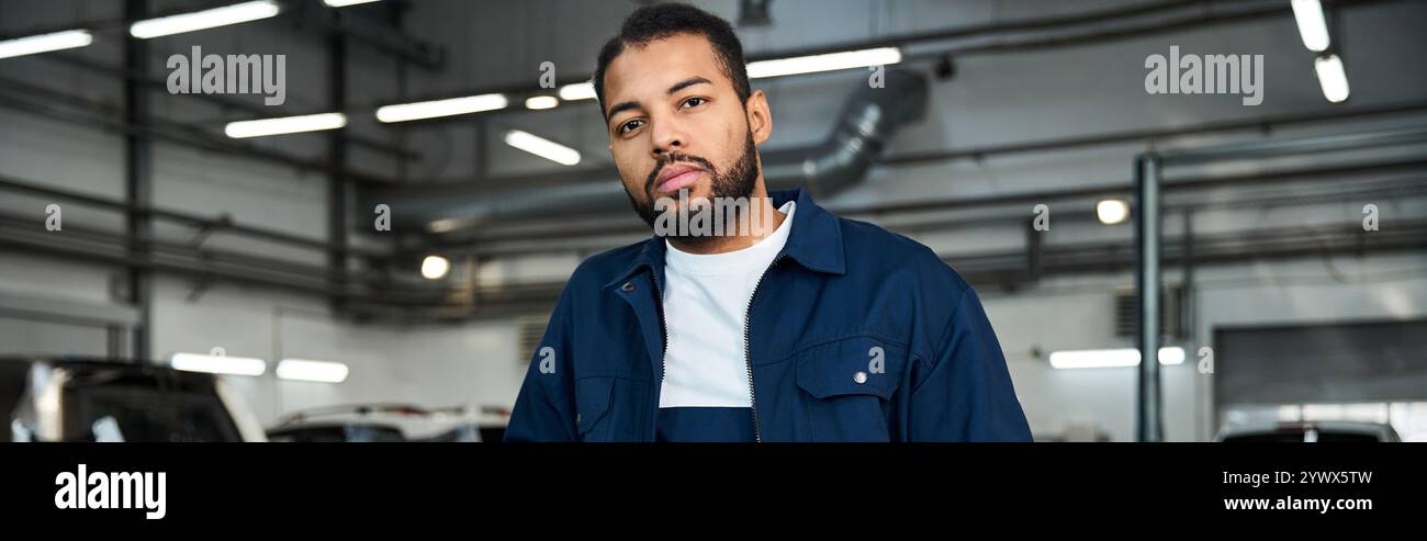 Ein hübscher junger Mann in mechanischer Uniform steht stolz in einer gut beleuchteten Automobilwerkstatt. Stockfoto