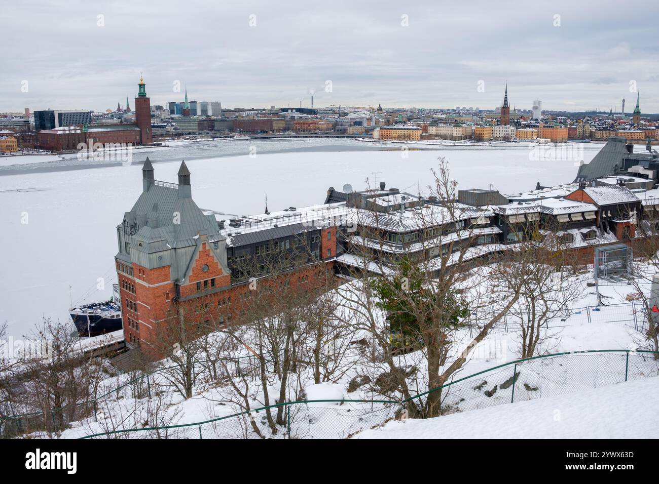 Stockholms Dächer sind mit Schnee bedeckt, während die gefrorenen Wasserstraßen eine ruhige Winteratmosphäre umgeben. Historische Architektur steht vor einem bewölkten Hintergrund. Stockfoto