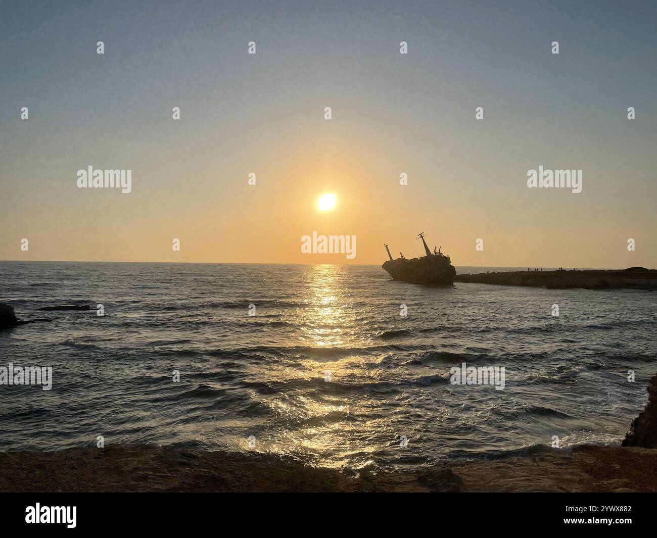Silhouette eines Schiffswracks vor dem Goldenen Sonnenuntergang über dem ruhigen Meer mit sanften Wellen, die das warme Licht Zyperns Ayia Napa reflektieren - Smartphone-aufgenommenes Stockfoto