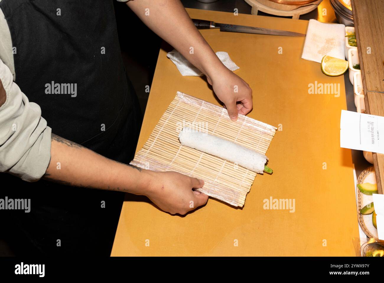 Nahaufnahme der Hände eines Küchenchefs, die vorsichtig eine Sushi-Rolle auf einer Bambusmatte Rollen Stockfoto