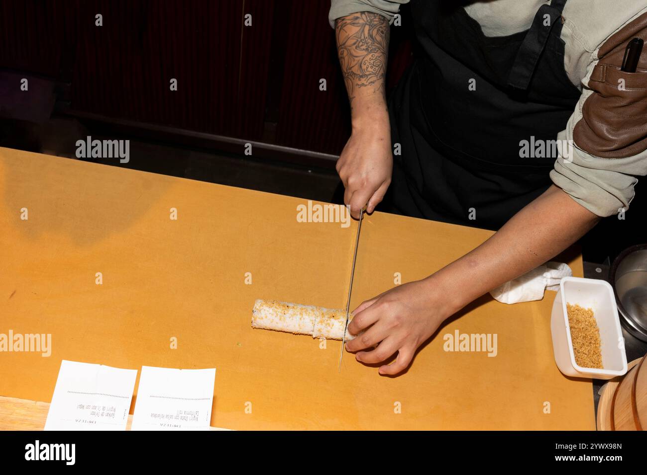 Nahaufnahme der Hände eines Küchenchefs, die vorsichtig eine Sushi-Rolle auf einem Brett schneiden. Stockfoto