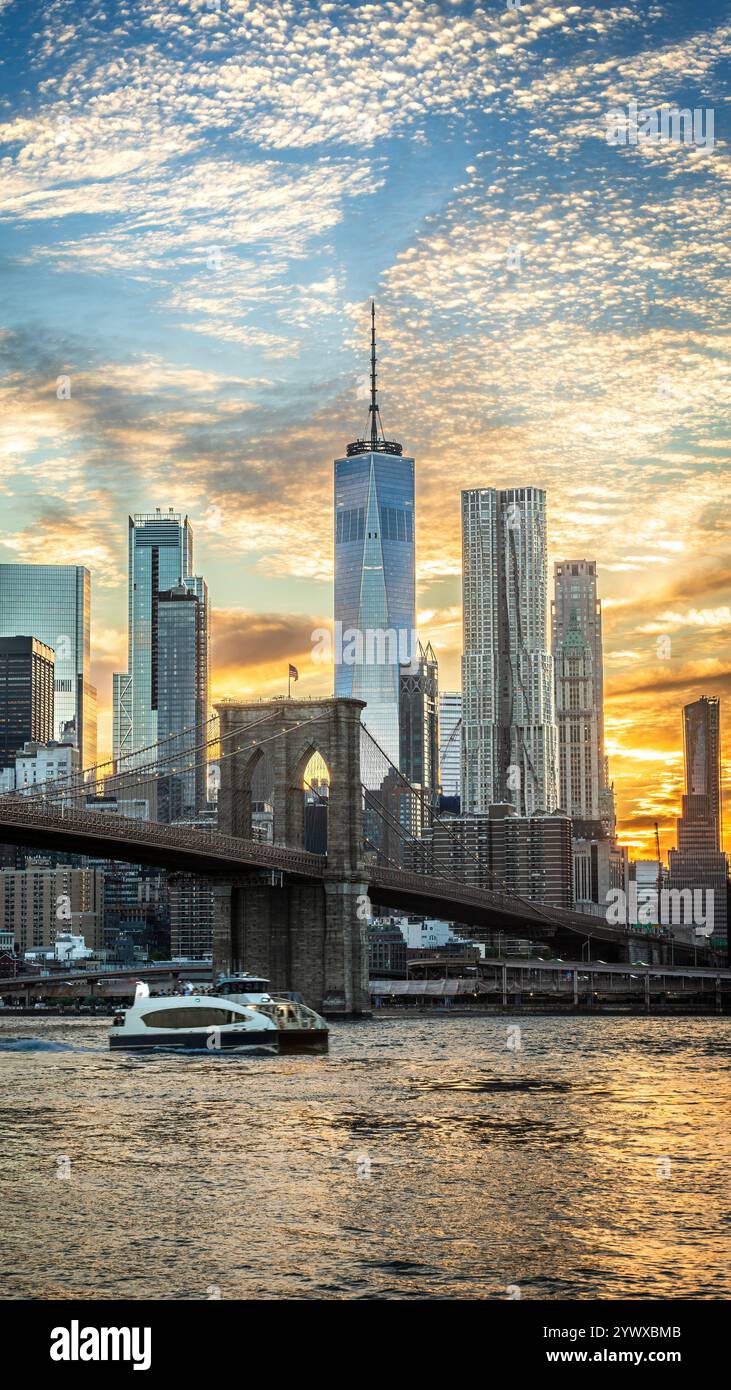 Das Foto zeigt die Brooklyn Bridge bei Sonnenuntergang von Brooklyn, wobei Wolken auf dem Wasser reflektieren. Die Skyline, ein moderner Wolkenkratzer im Hinterland Stockfoto