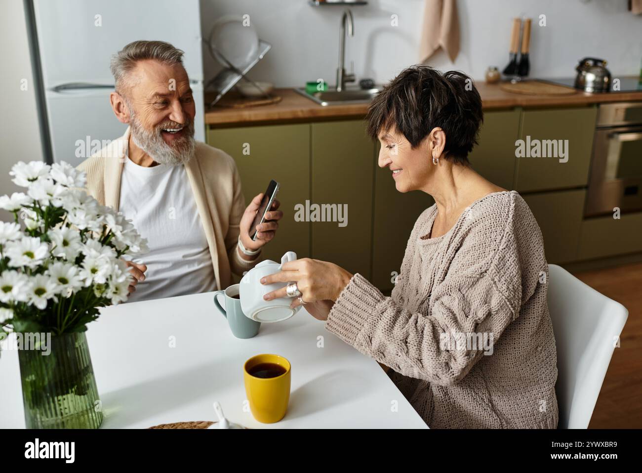 Ein fröhliches, reifes Paar teilt sich einen Moment des Lachens, während er gemeinsam Kaffee genießt. Stockfoto