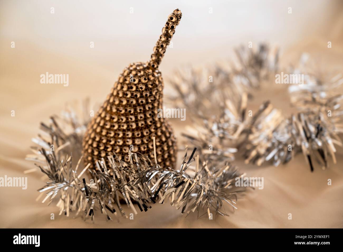 Goldene dekorative Metallbirne und glänzende Silberkette, dekoratives Weihnachtsobjekt, Stillleben auf hellem beigem Hintergrund. Nahaufnahme. Stockfoto
