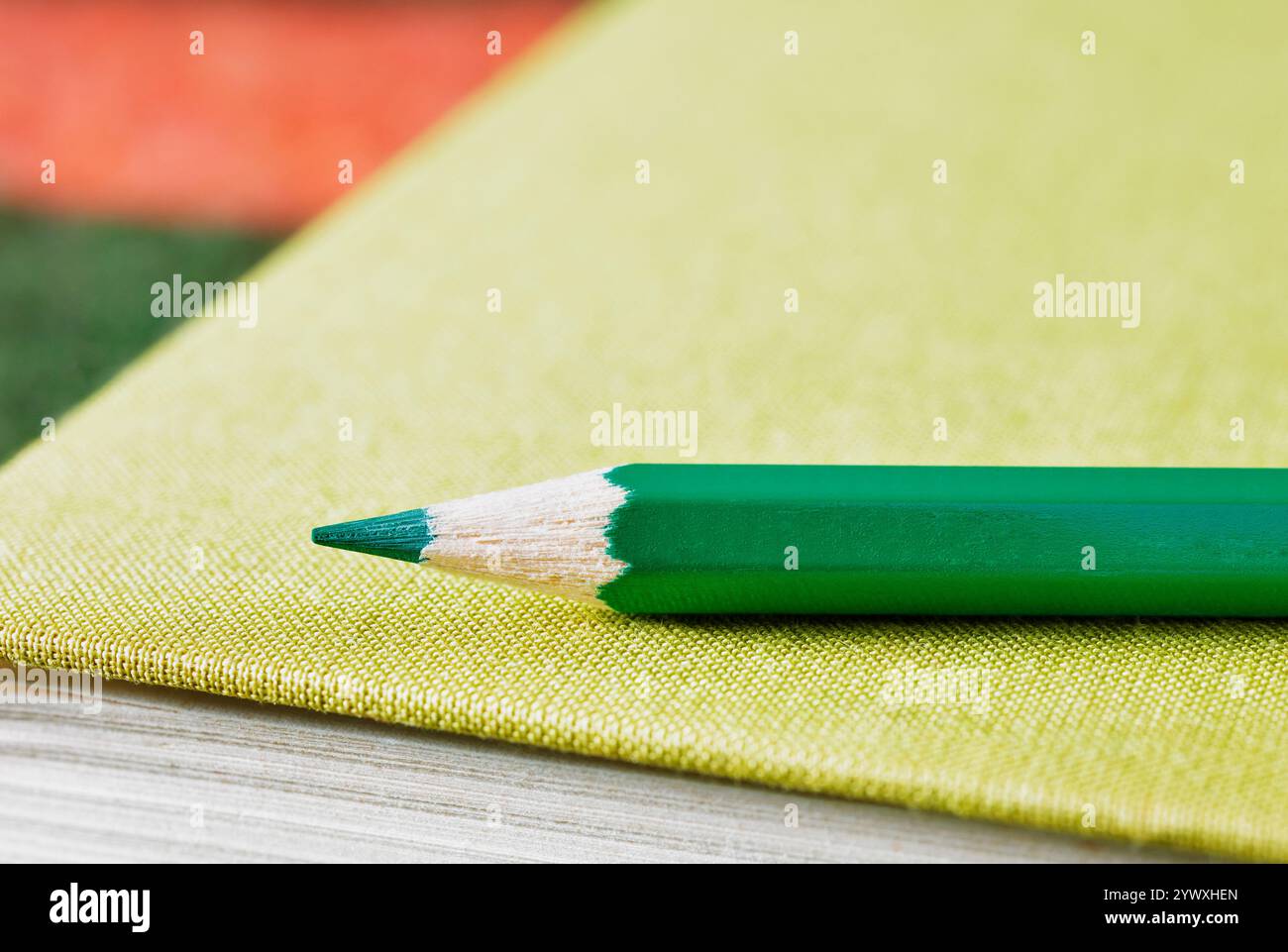 Spitzer grüner Holzstift auf grünem Hardcover-Buch, Ort der Arbeit oder Freizeit Stockfoto