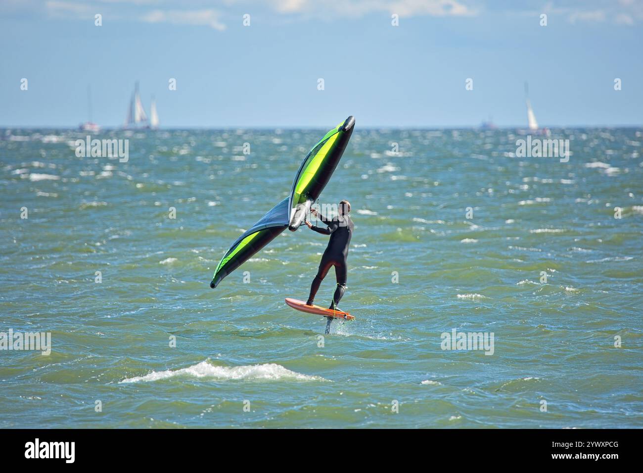 Der Mann ist Flügelfolierung mit handgehaltenem aufblasbarem Flügel und Tragflächensurfbrett im Meer im Sommer. Fahrer auf einem Windflügel-Board, surft in den Wellen. Stockfoto