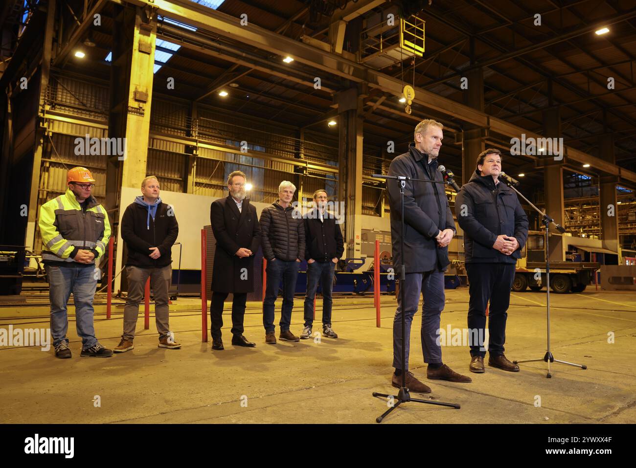 12. Dezember 2024, Schleswig-Holstein, Flensburg: Die vorläufigen Insolvenzverwalter Christoph Morgen (r) von der Anwaltskanzlei Brinkmann Partner und Hendrik Gittermann von der Anwaltskanzlei Reimer Rechtsanwälte sprechen auf einer Pressekonferenz in einer Schiffshalle der FSG nach einer Mitarbeiterversammlung. Für die beiden Schleswig-holsteinischen Werften FSG (Flensburg) und Nobiskrug (Rendsburg), die zur Werftgruppe des Investors Lars Windhorst gehören, wurde Insolvenz beantragt. Dahinter stehen Marcus Stöcken (l-r), Chef des betriebsrats Nobiskrug, Jan Brandt, Leiter des betriebsrats der FSG (Flensburger Schiffbau Gesell) Stockfoto