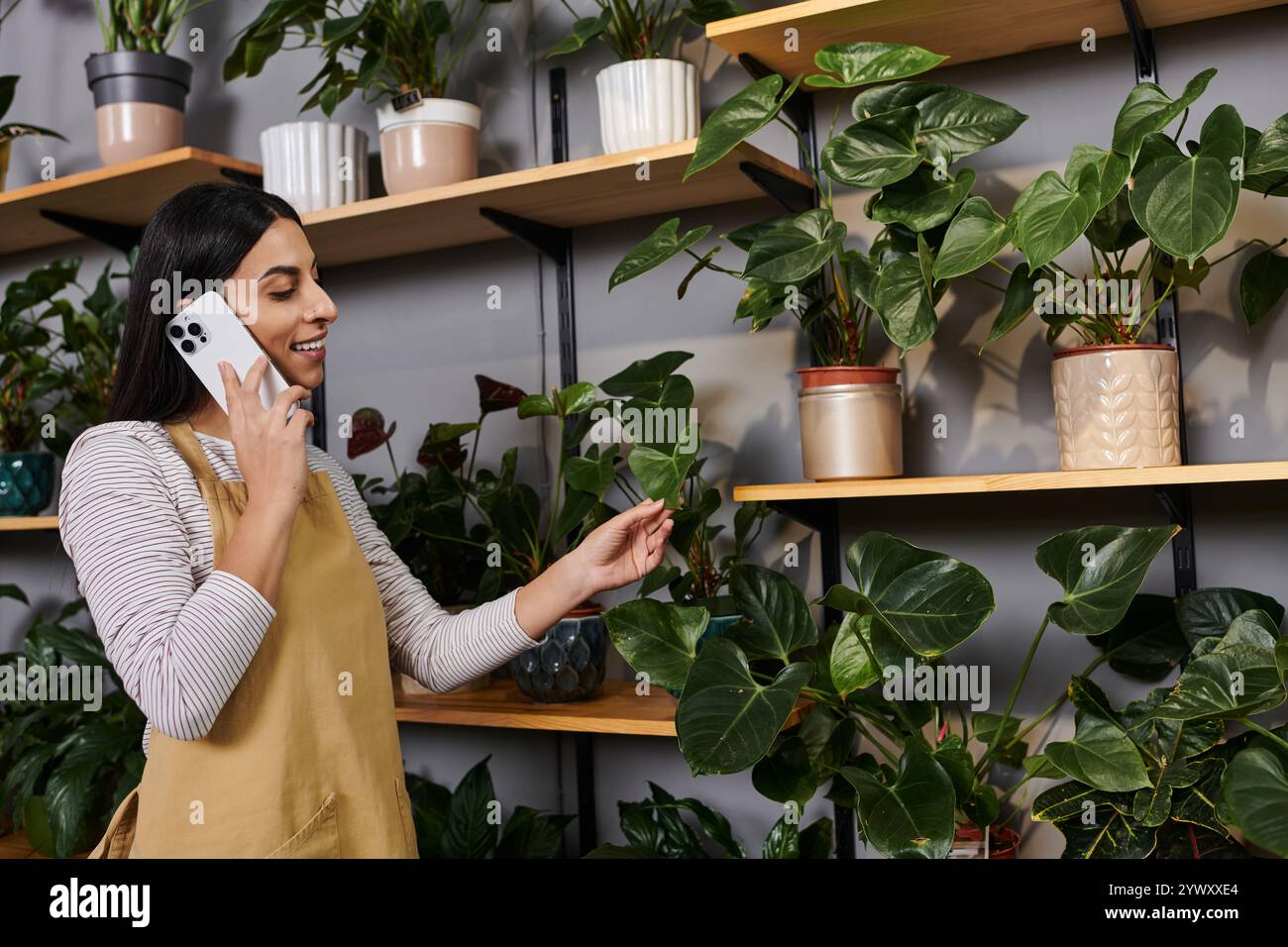 Eine junge Floristin arrangiert gerne Pflanzen, während sie in ihrem Geschäft telefoniert. Stockfoto