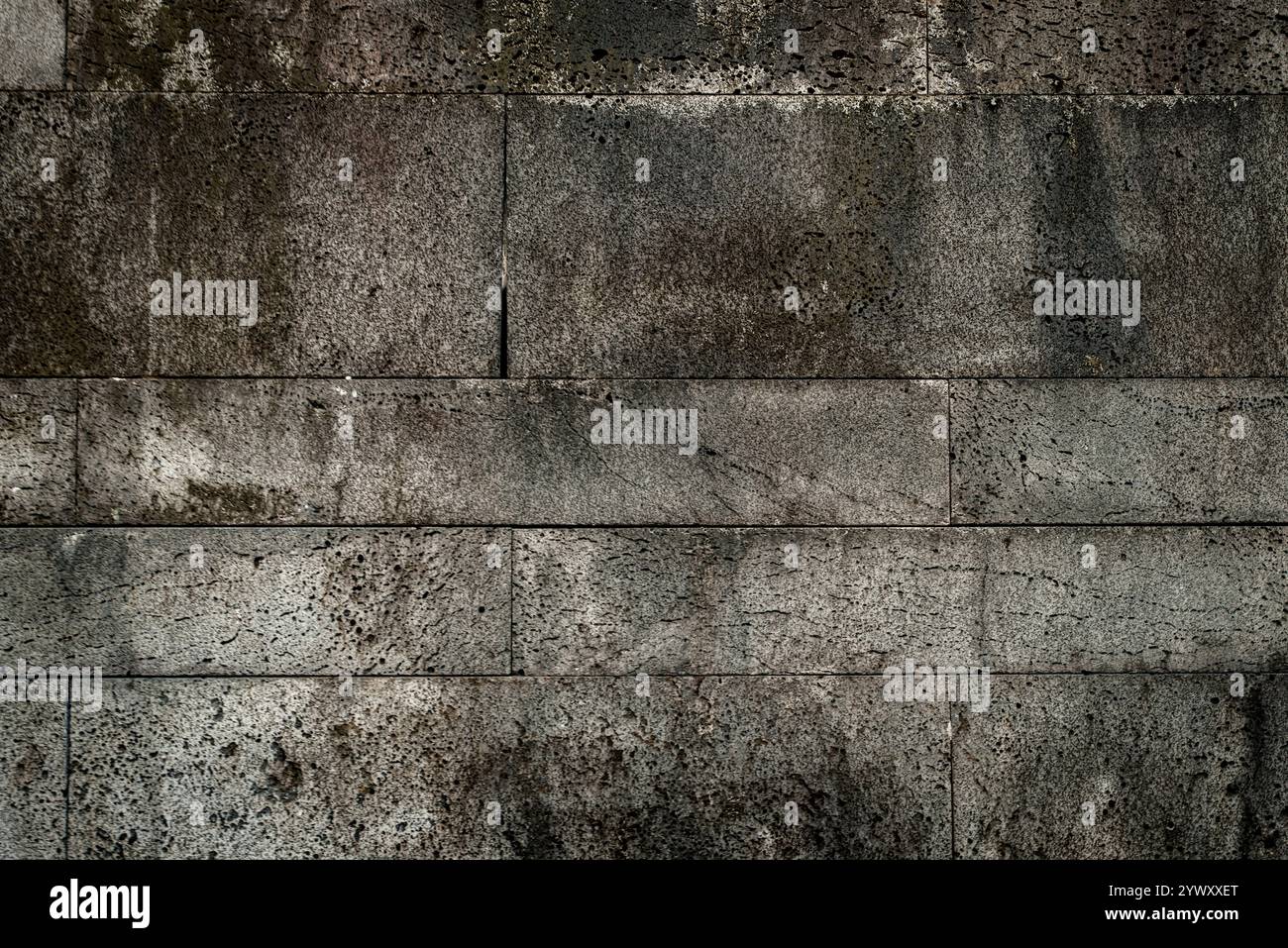 Eine Wand aus Stein mit einer grauen Farbe. Die Mauer ist alt und hat viele Risse Stockfoto