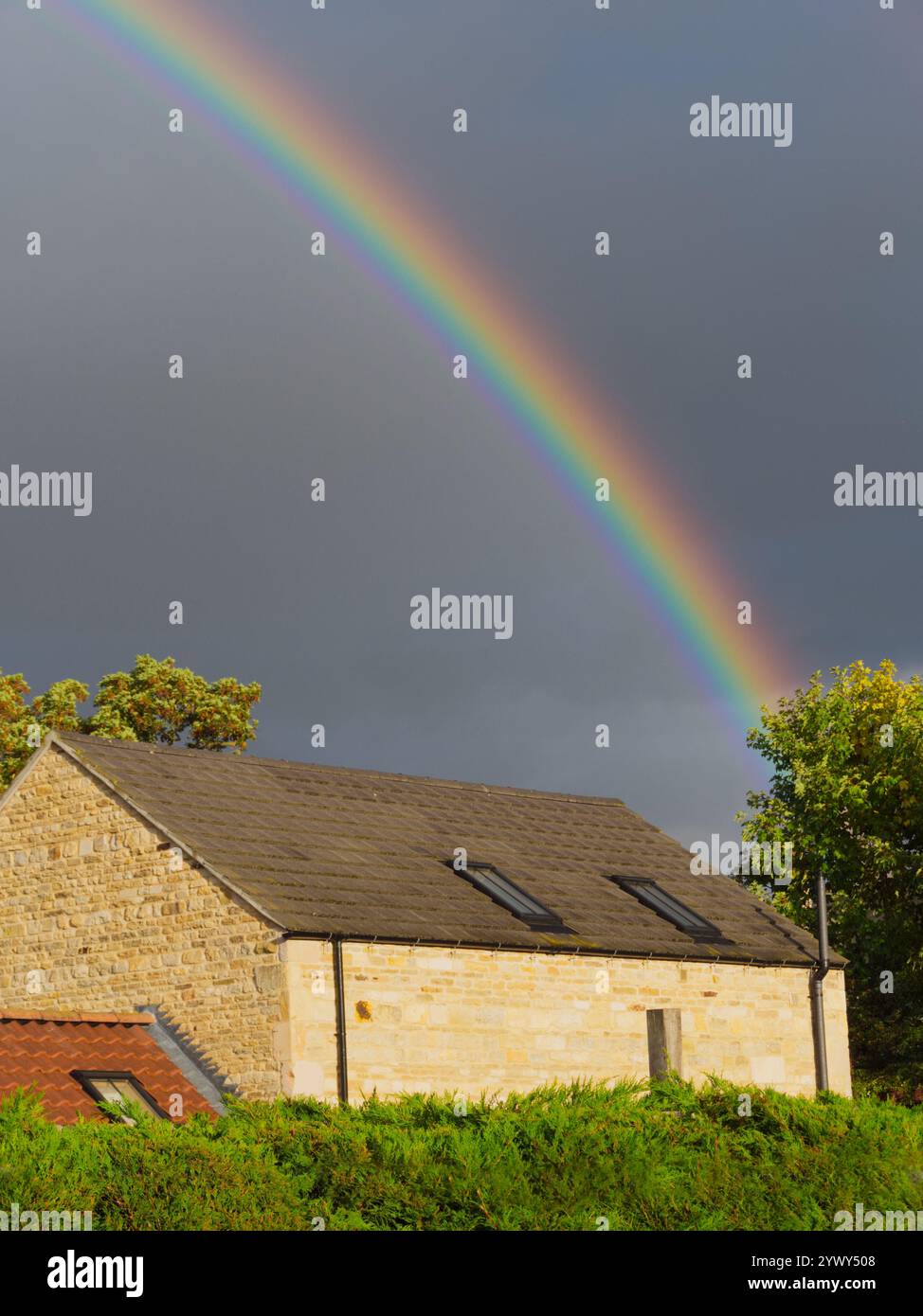 Der Bogen eines wunderschönen Regenbogens an einem grauen oder grauen Himmel, über einer alten Steinscheune, im warmen Licht des Herbstes oder Herbstes. Stockfoto