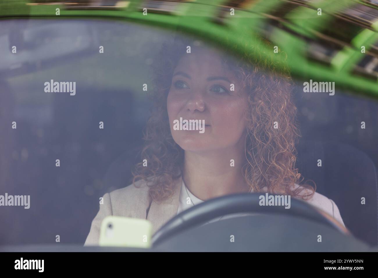 Eine Frau mit lockigen Haaren wird durch die Windschutzscheibe eines Autos gesehen und konzentriert sich auf das Fahren. Das Bild unterstreicht die Bedeutung von Verkehrssicherheit und Verantwortung Stockfoto