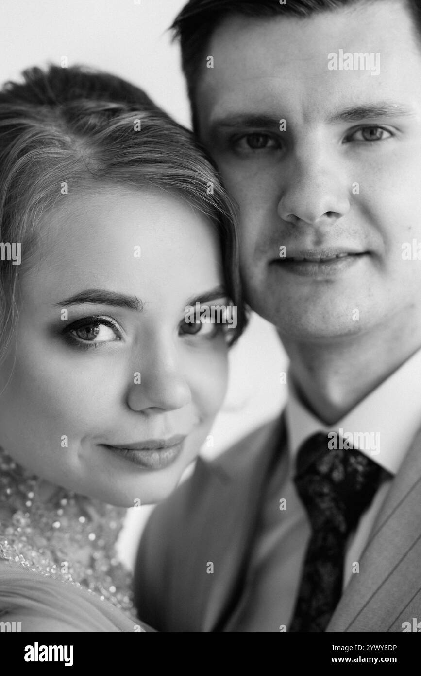 Bräutigam in beigem Anzug und Braut in lavendelfarbenem Hochzeitskleid in hellem Studio Stockfoto