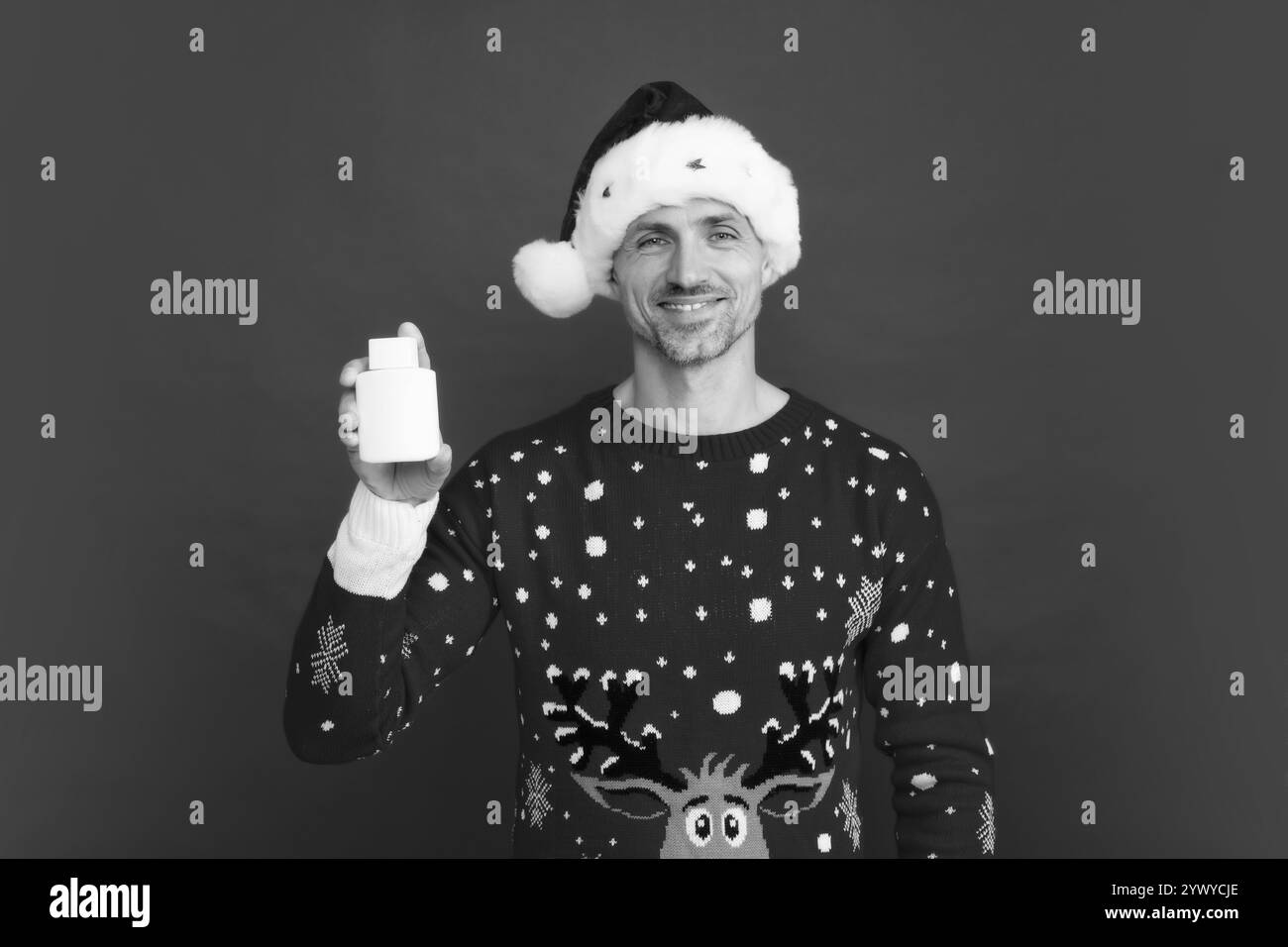 Ein hübscher Mann im Winterpullover und der Weihnachtsmann hat eine Flasche Medizin auf Studio-rotem Hintergrund. Stockfoto