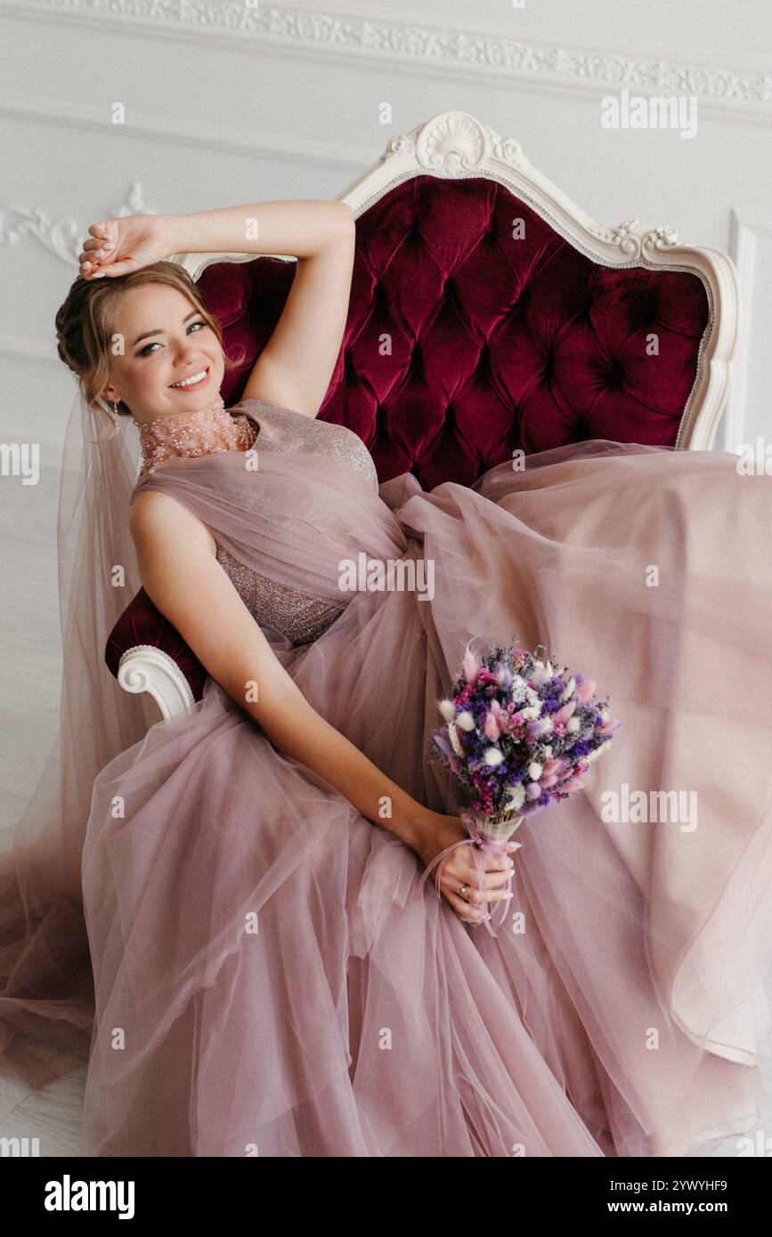 Braut in flauschigem Hochzeitskleid in hellem Studio mit Blumenstrauß Stockfoto