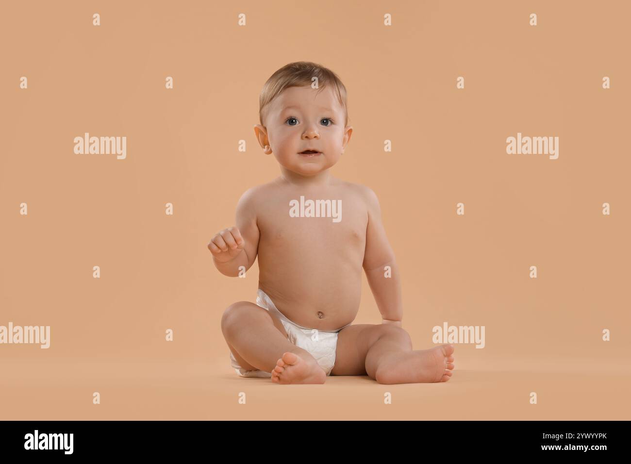 Niedliches kleines Baby in Windel, das auf beigefarbenem Hintergrund sitzt Stockfoto