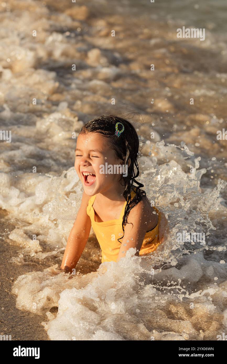 Glückliches Kleinkind lacht und spielt mit Wellen am Ufer an sonnigen Tagen, Sommerurlaub und Kindheitserinnerungen Konzept - Bild Stockfoto