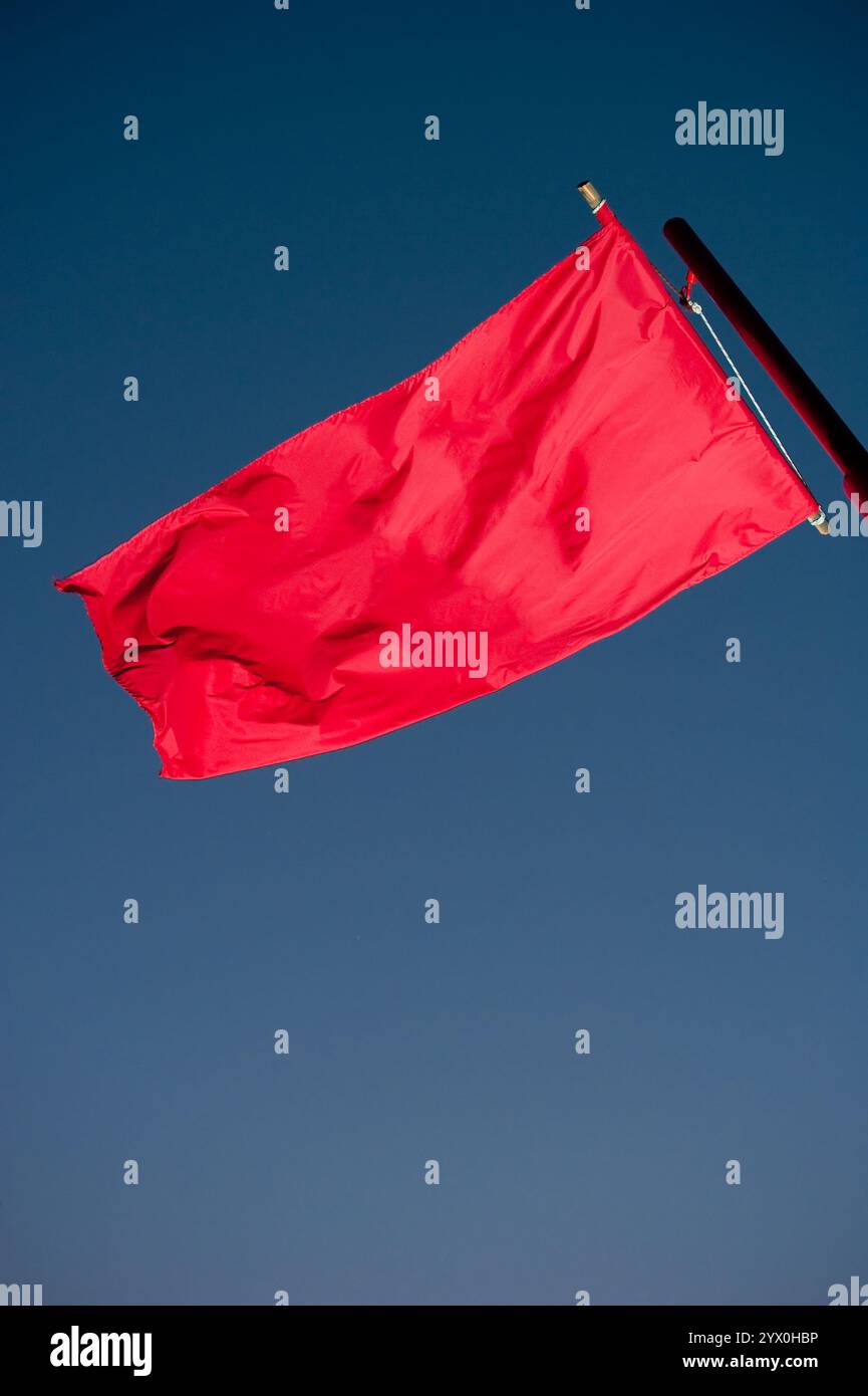 Rote Flagge, die auf dem Wind fliegt, mit blauem Himmel im Hintergrund Stockfoto