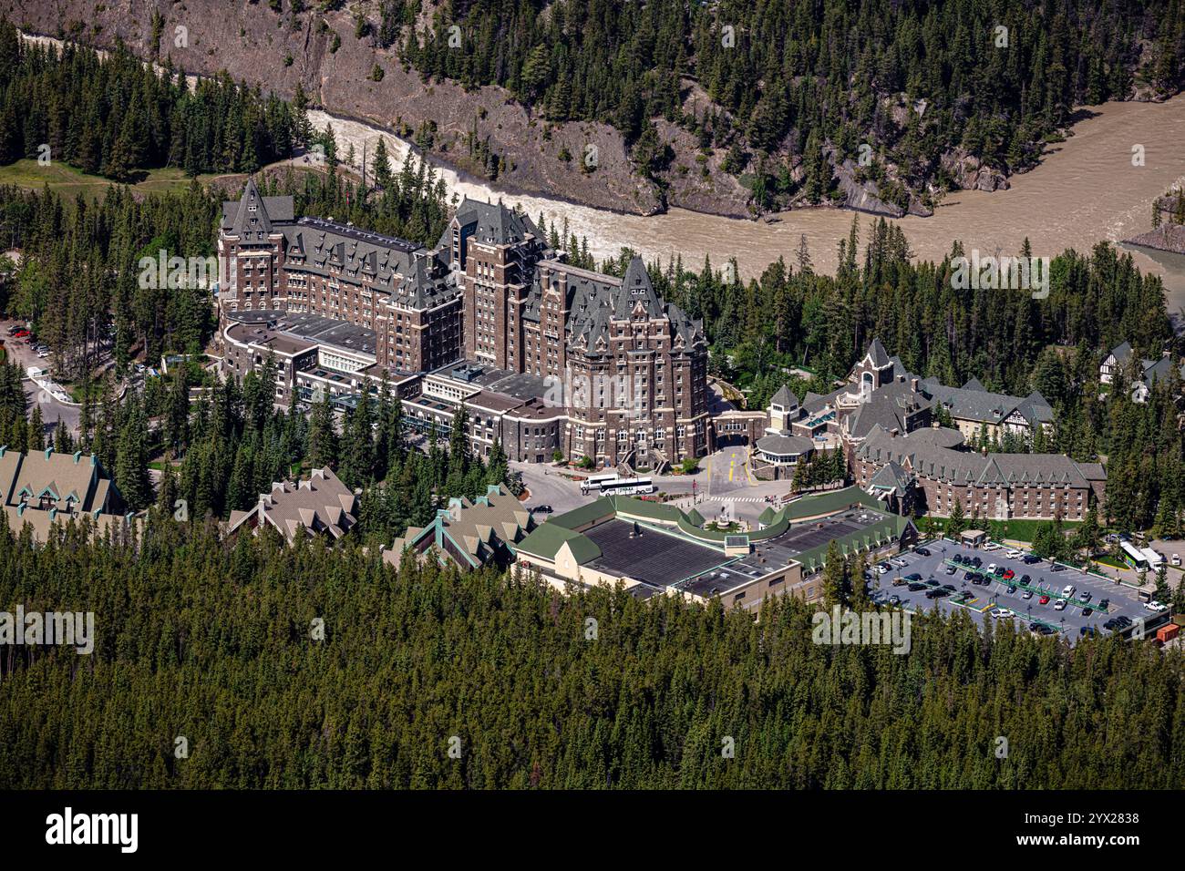 Ein großes Hotel mit vielen Bäumen im Hintergrund. Das Hotel ist von einem Wald umgeben und hat einen Fluss, der durch ihn fließt Stockfoto