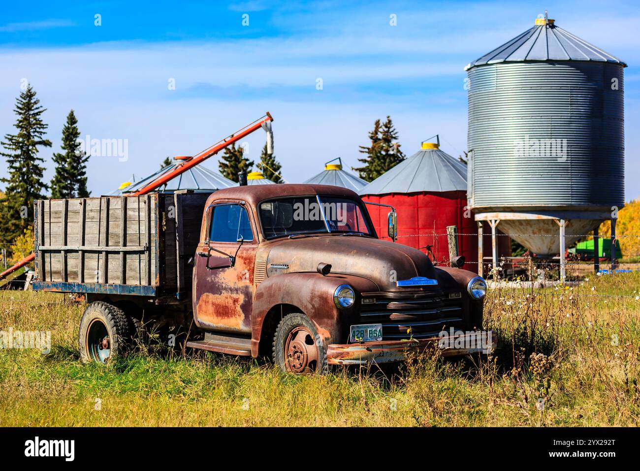 Ein alter Lkw steht auf einem Feld neben einem Silo. Der Stapler ist rostfrei und hat viel Charakter. Das Silo ist hoch und metallisch, und es ist umgeben Stockfoto