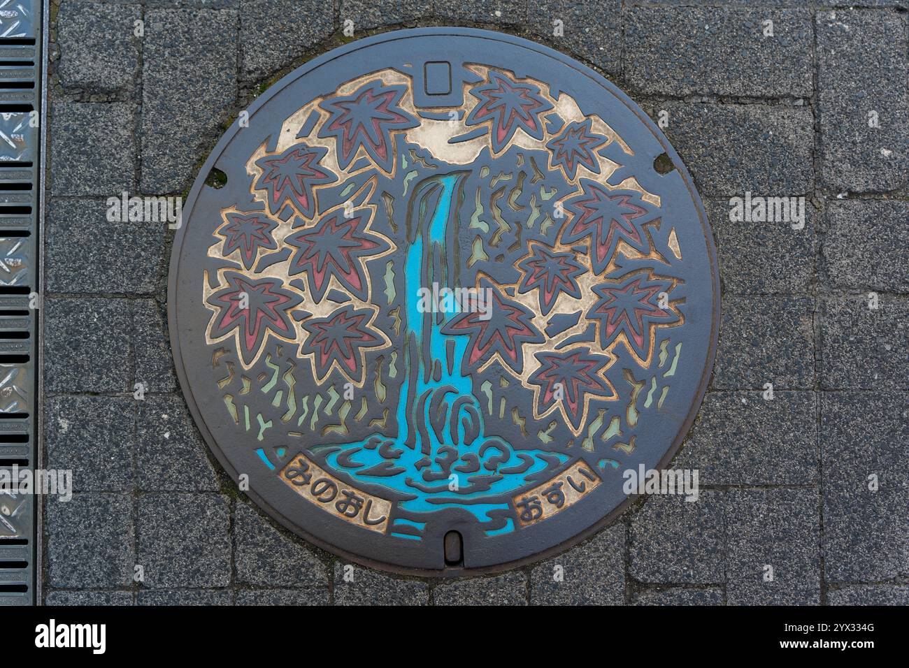 Ein farbenfrohes Mannlochdesign mit Wasserfall und herbstlichen Ahornblättern in Minoh City, Osaka, Japan. Übersetzung: Minoh City Water Supply. Stockfoto