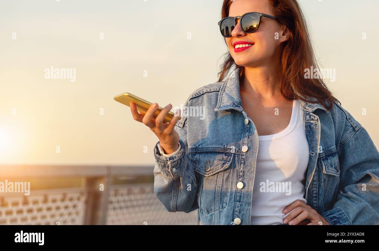 Junge urbane Frau in lässigem Outfit, die ihr Smartphone hält, geht draußen. Stockfoto