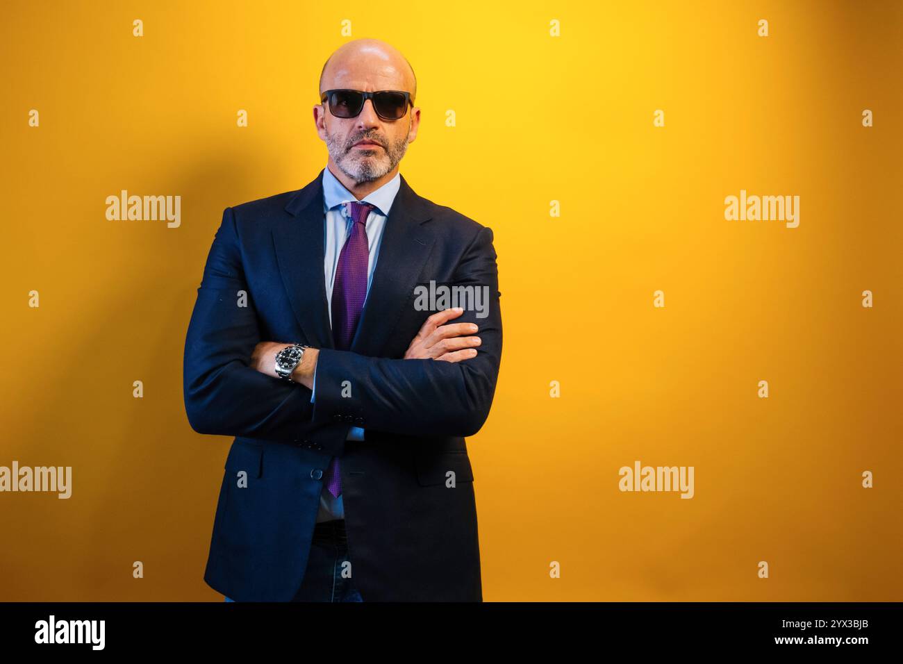 Ein Mann in Anzug und Sonnenbrille steht vor einer gelben Wand. Stockfoto