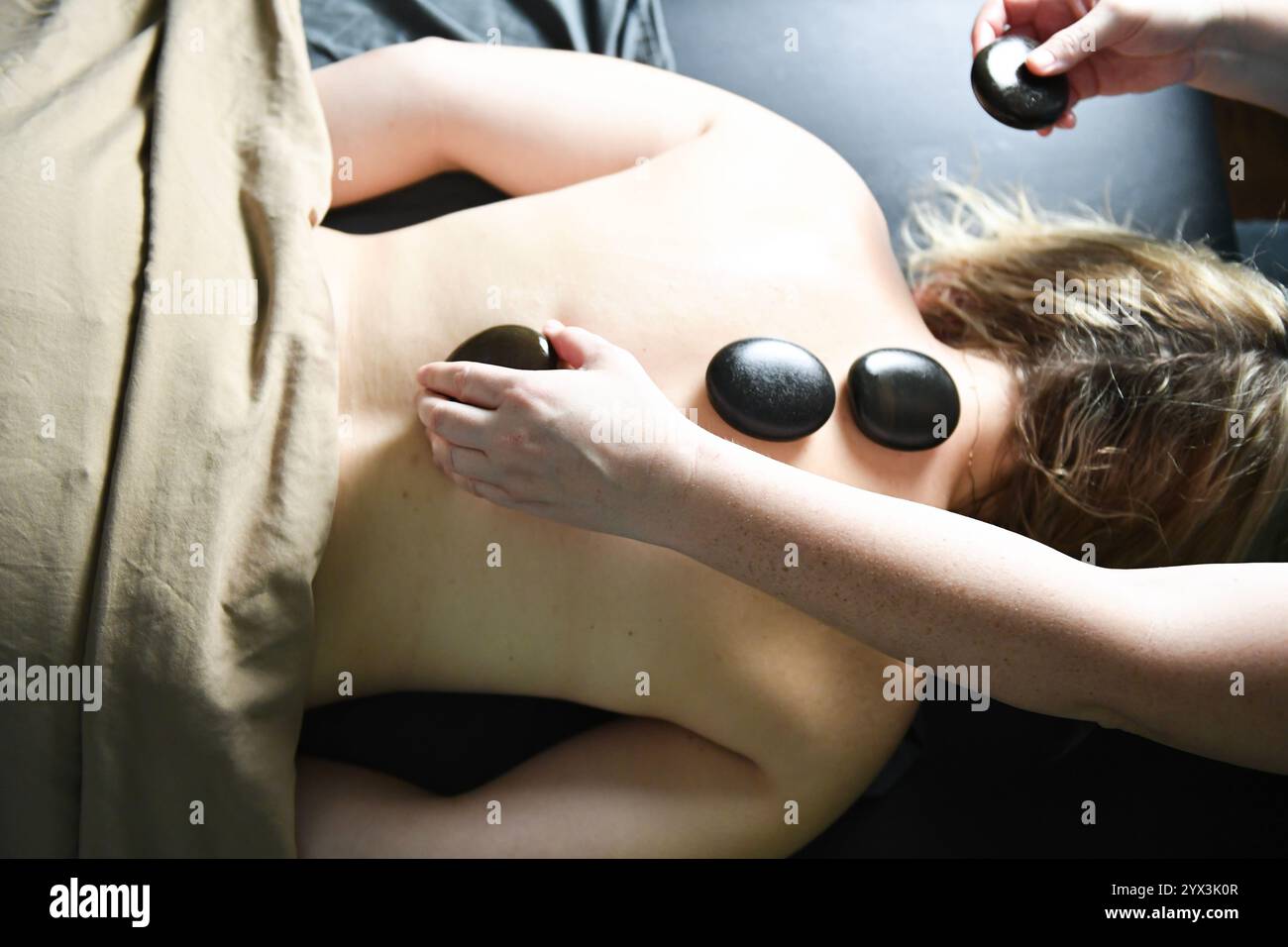 Hot-Stone-Massagetherapie mit glatten schwarzen Steinen auf Ba Stockfoto