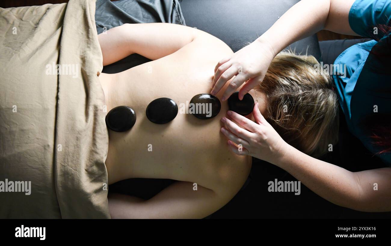 Heiße Steine, die sich auf dem Rücken eines Kunden während eines entspannenden Wellnessbereichs ausrichten Stockfoto