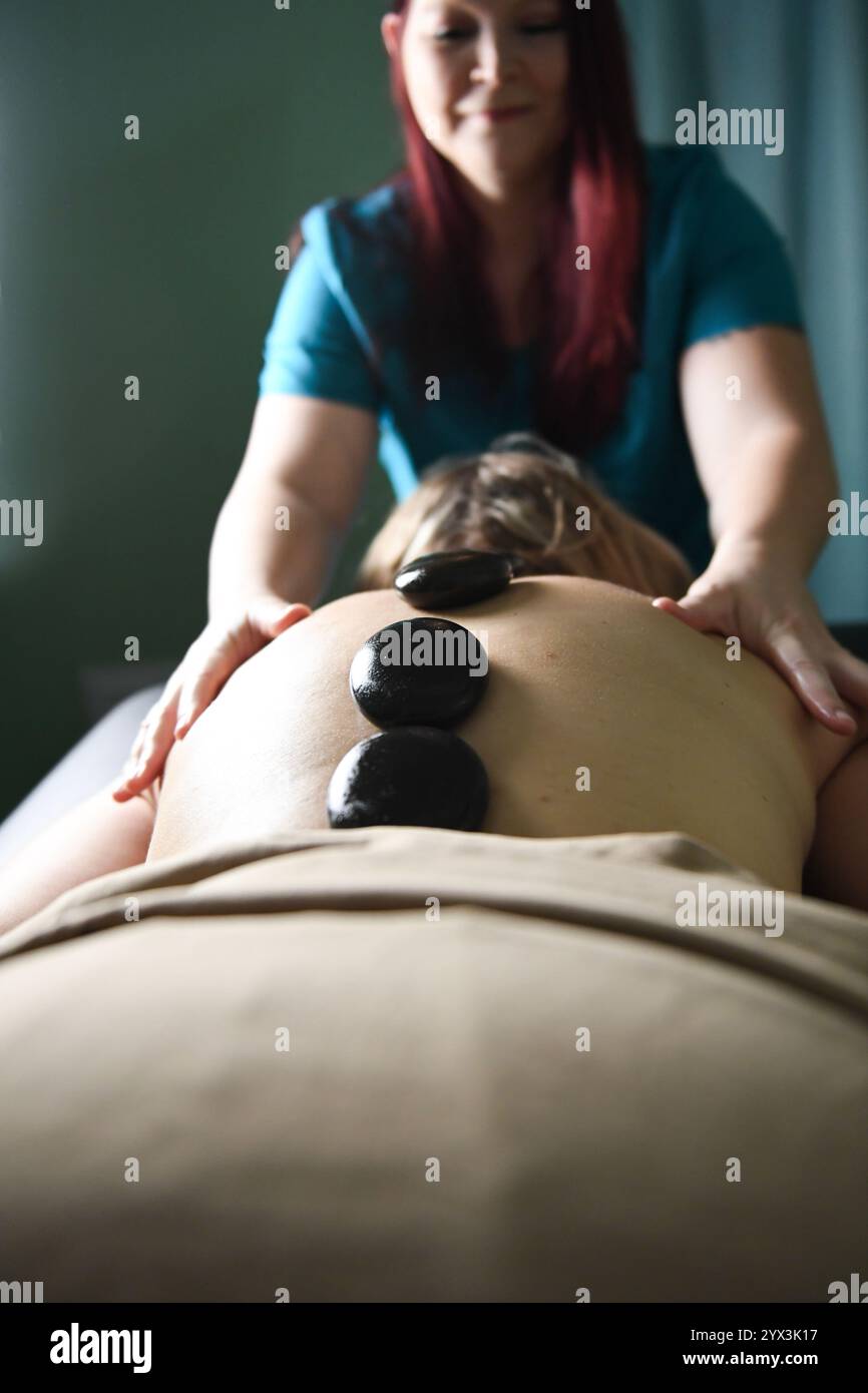 Heiße Steine, die während einer wohltuenden Massagetherapie auf den Rücken gelegt werden Stockfoto