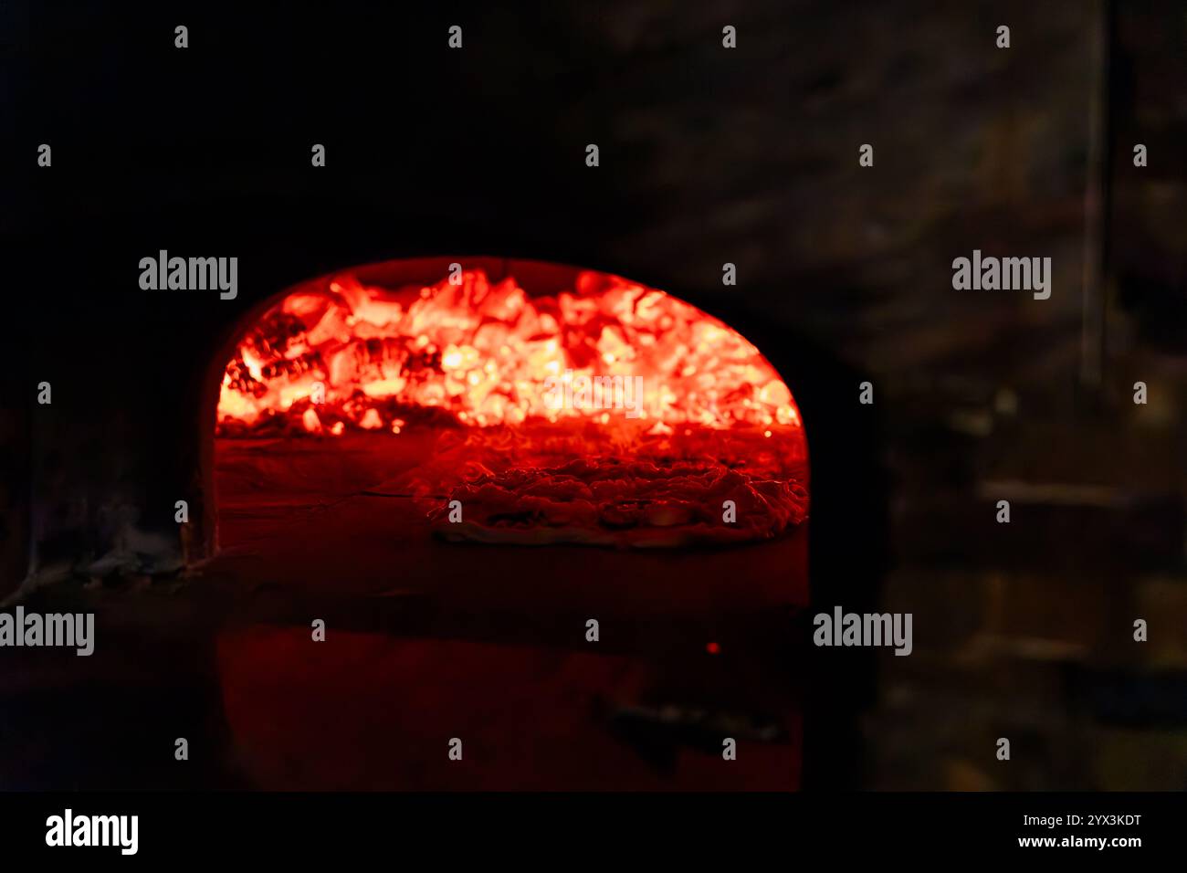 Eine Pizza, die in einem glühenden Holzofen mit intensiver Glut gebacken wird Stockfoto