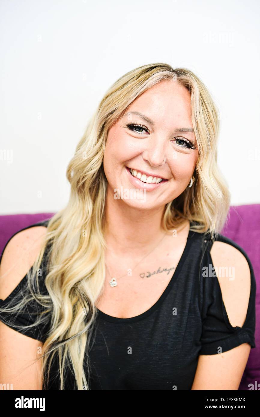 Lächelnde blonde Frau mit welligen Haaren und einem schwarzen Hemd, Nahaufnahme. Stockfoto