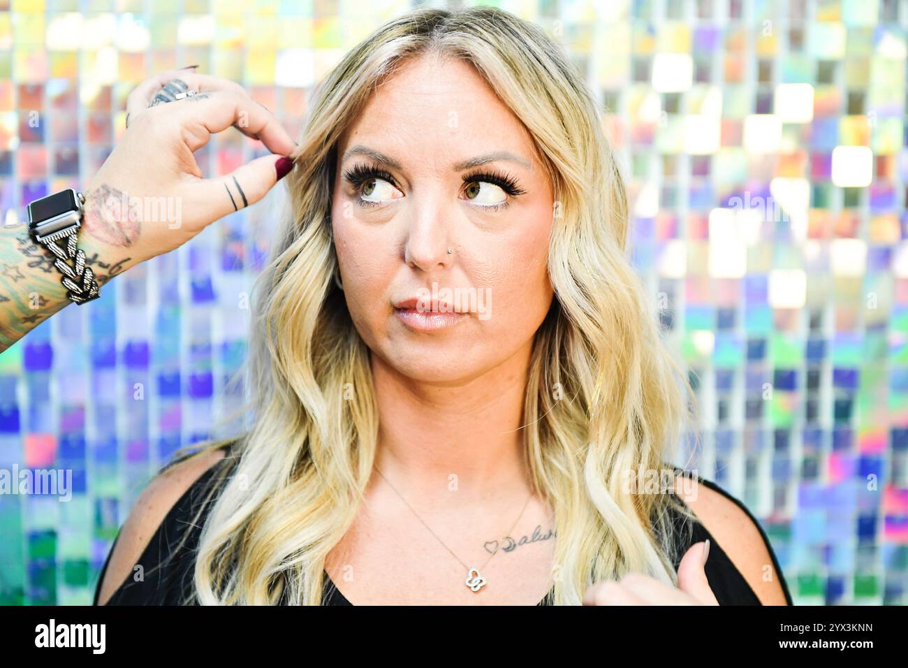 Frau mit blondem, gewelltem Haar, die Hand des Stylisten passt die Stränge an. Stockfoto