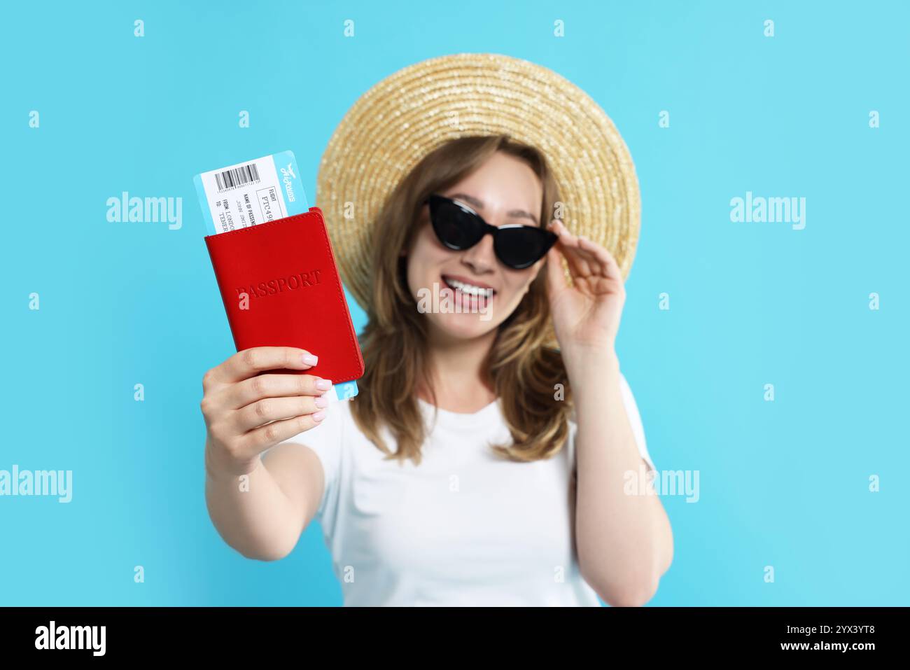 Glücklicher Reisender in Sonnenbrille mit Pass und Ticket auf hellblauem Hintergrund, selektiver Fokus Stockfoto
