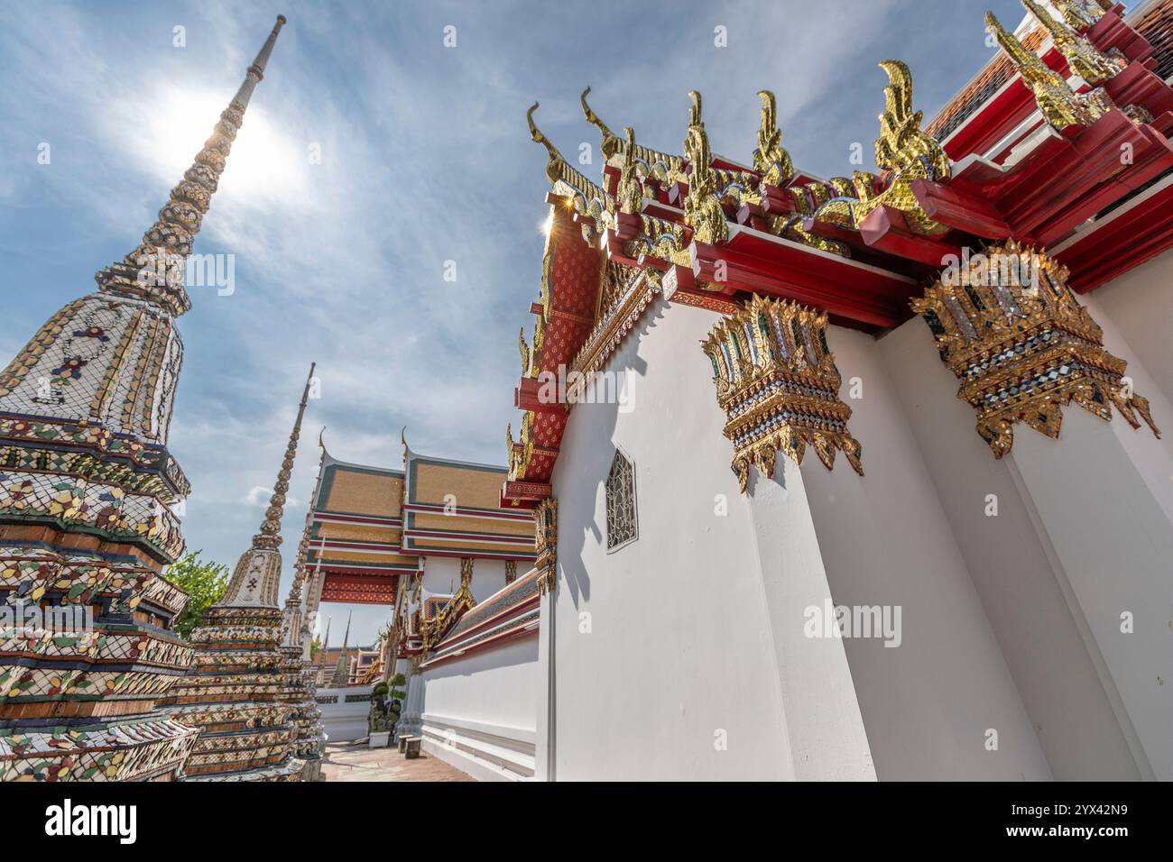 Niedrigwinklige Ansicht eines keramikverkleideten Chedi und aufwendiger Dachverzierungen über einer weißen Tempelmauer im Wat Pho, Bangkok, Thailand Stockfoto