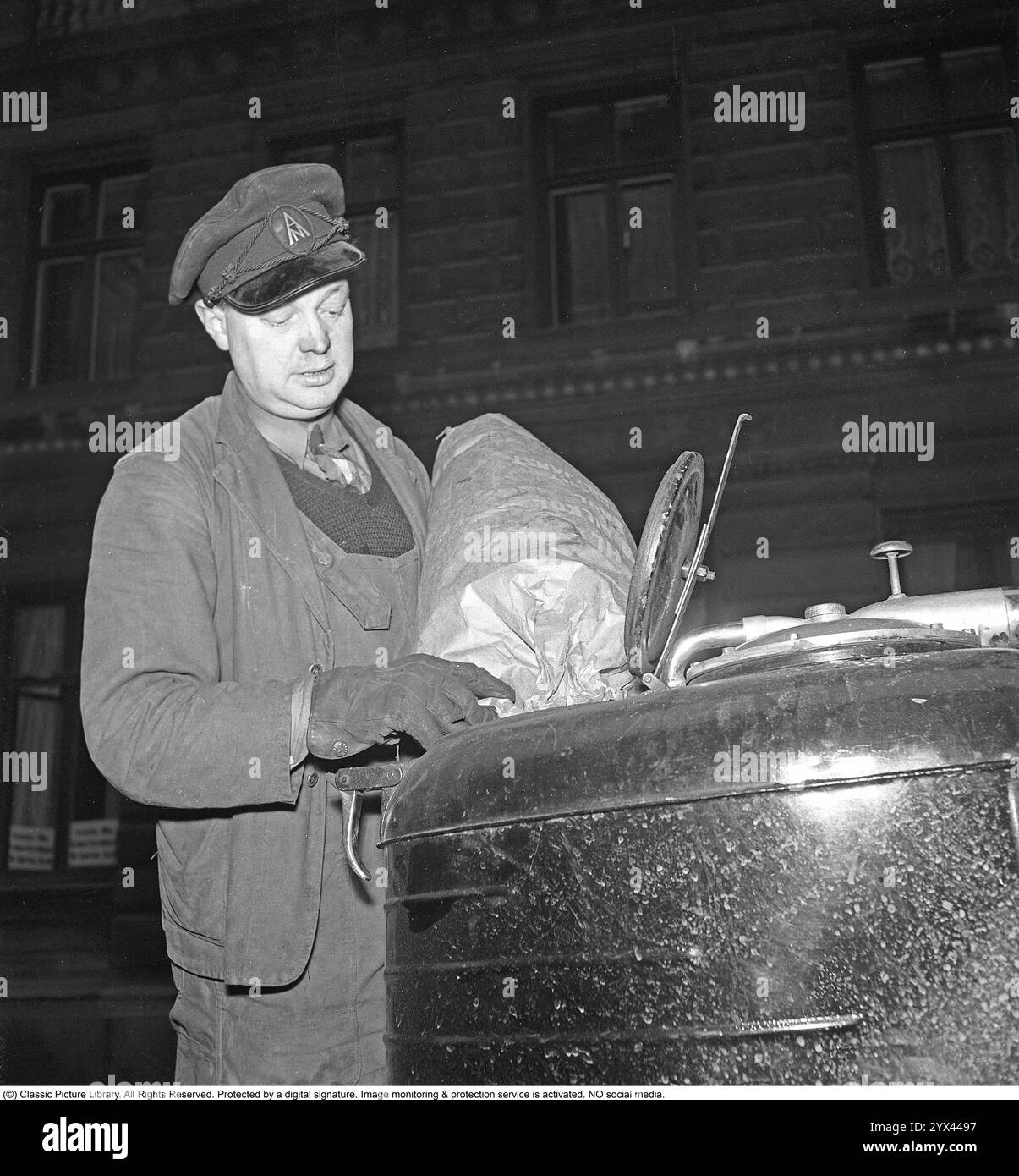 Holzgas 1942. Ein Mann füllt mehr Kohle in den Container, um die Holzgaseinheit seines LKW zu betanken. Ein natürliches Merkmal während dieser Jahre während des Zweiten Weltkriegs war die Wood-Vergasungseinheit auf Autos und Lkws. Holzgas ist ein Gas, das bei der unvollständigen Verbrennung von Holz oder Kohle entsteht und zum Antrieb von Fahrzeugen verwendet wurde. Der Fahrer musste die Kohle selbst auffüllen und sicherstellen, dass die Verbrennung ordnungsgemäß funktioniert. Aufgrund des Treibstoffmangels während des Zweiten Weltkriegs spielte Holzgas eine wichtige Rolle für den Fortbestand des Transports. Kristoffersson Ref. A124-6 Stockfoto