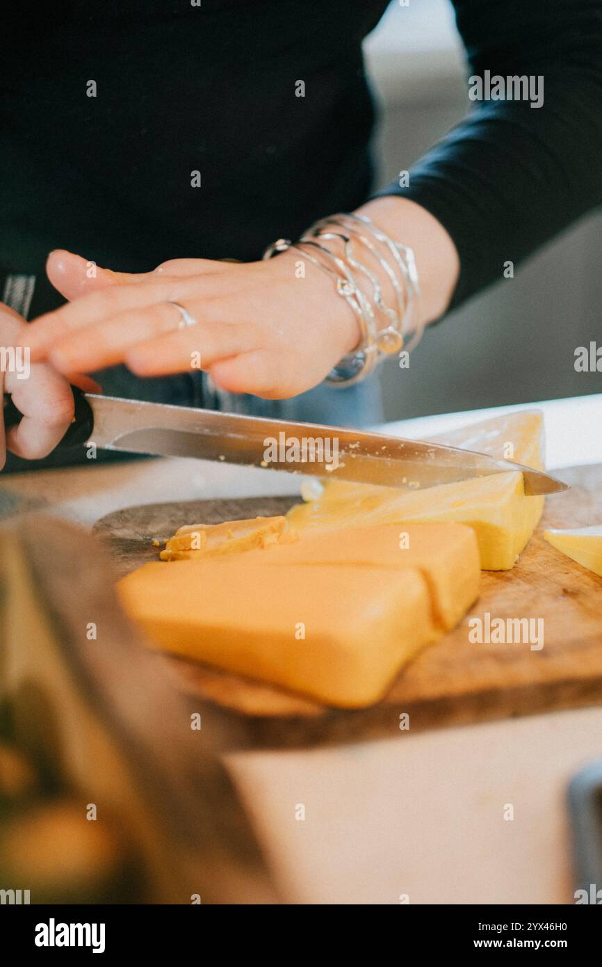 Eine Frau schneidet ein Stück Käse auf einem Schneidebrett. Sie trägt einen Ring und Armbänder Stockfoto